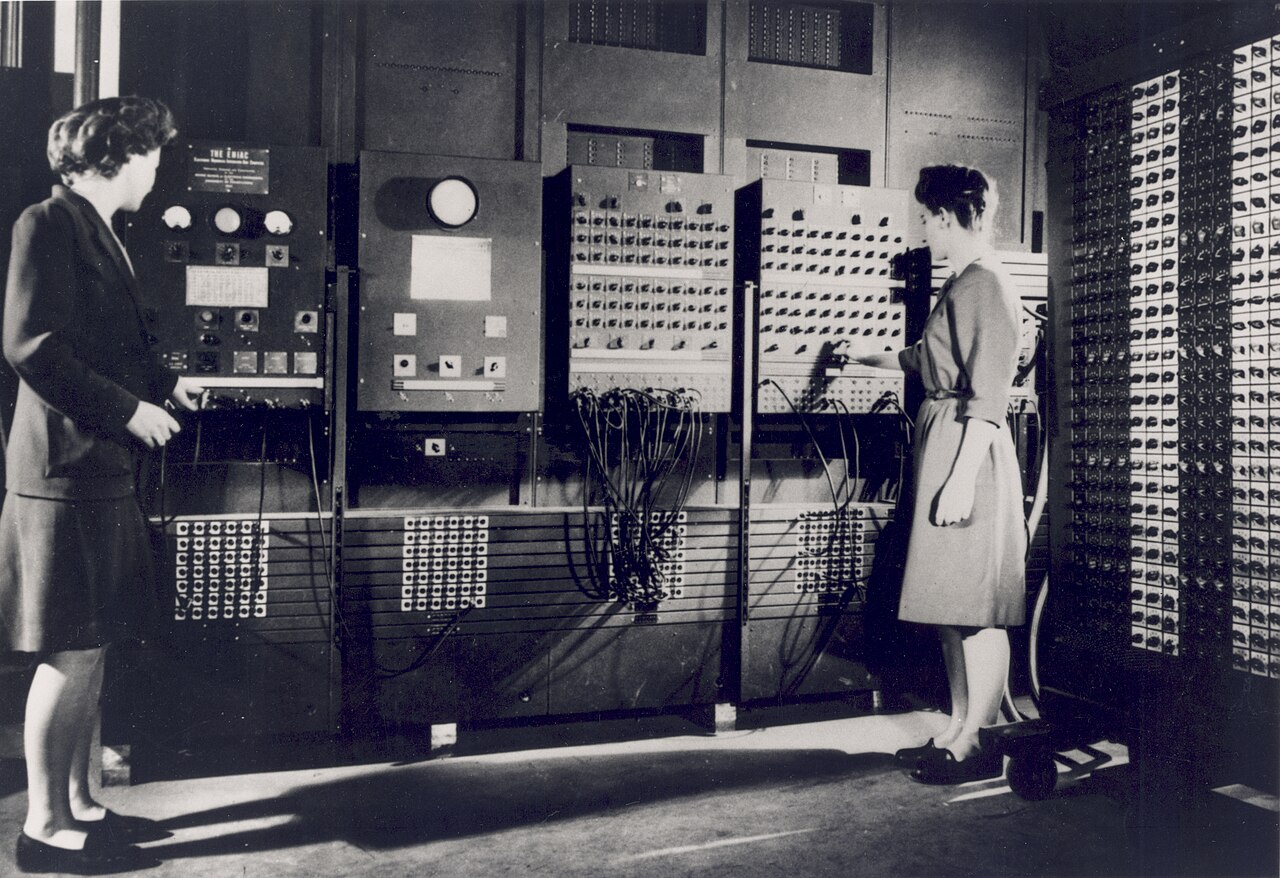 Betty Jean Jennings à esquerda e Frances Bilas à direita, de pé diante dos painéis do ENIAC, ligando cabos, em 1946.